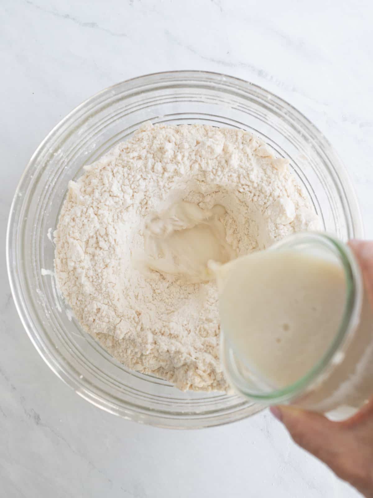 Buttermilk being poured into biscuit ingredients in a mixing bowl.