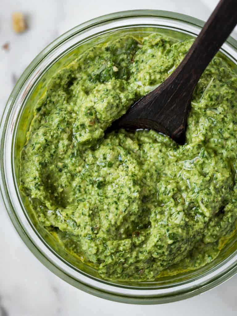 Silky smooth basil pesto in a jar with a spoon.