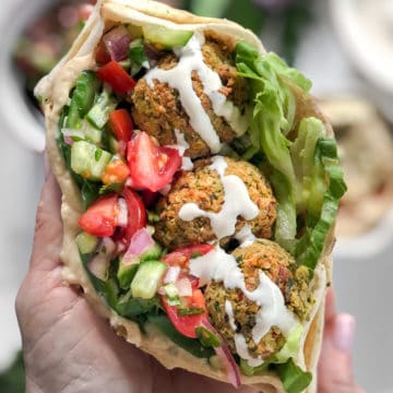 Vegan falafel wrap with tomatoes hummus and cucumbers in a pita with tahini sauce.