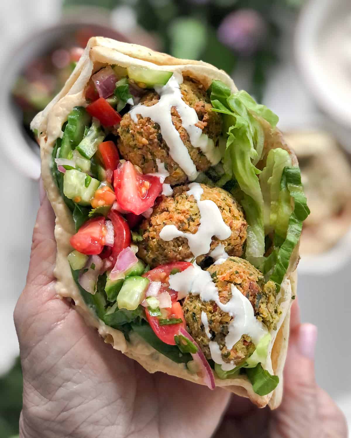 Vegan falafel wrap with tomatoes hummus and cucumbers in a pita with tahini sauce.