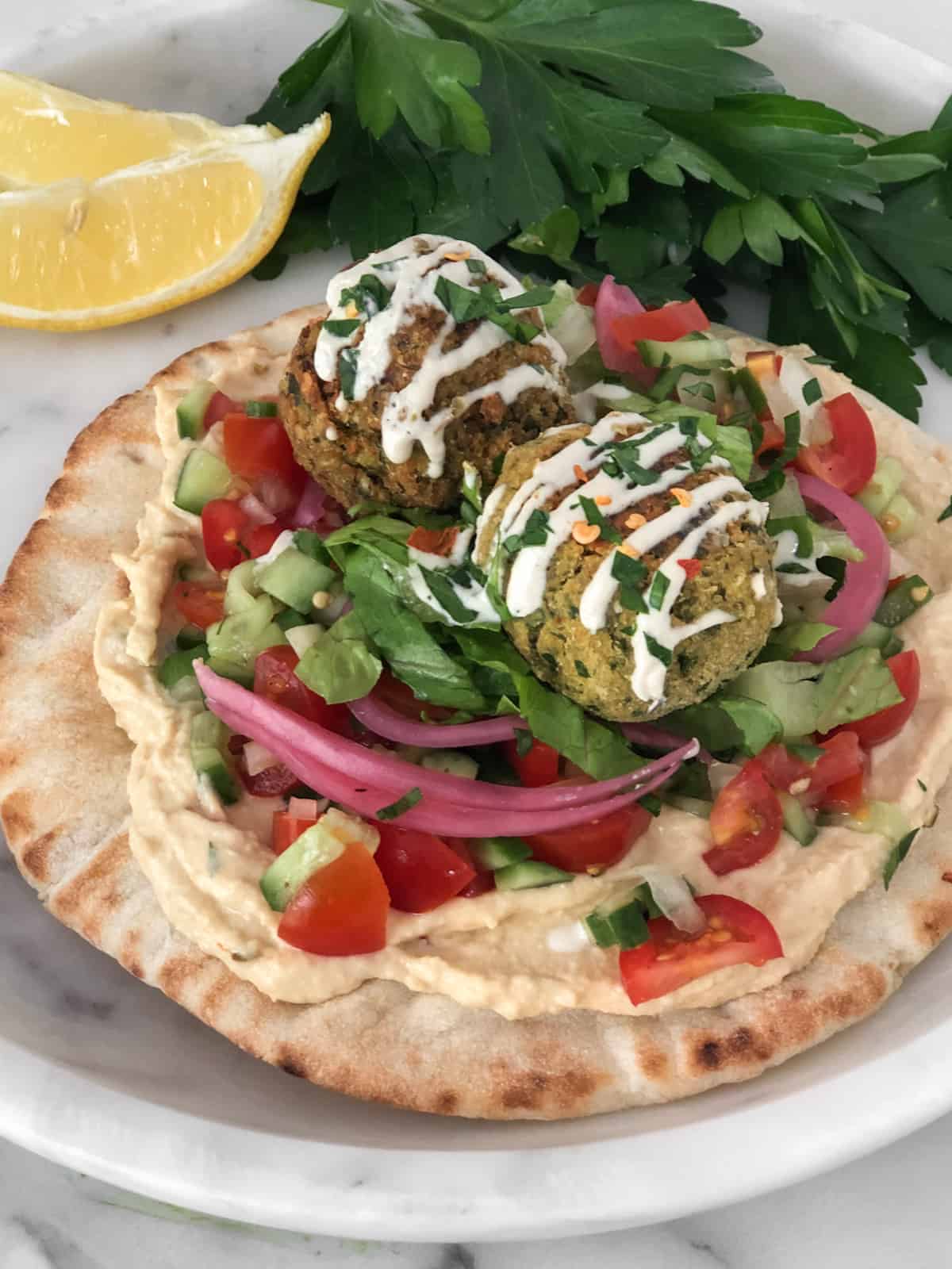 Pita topped with hummus, tomato, cucumber, pickled onions, falafel and tahini sauce.