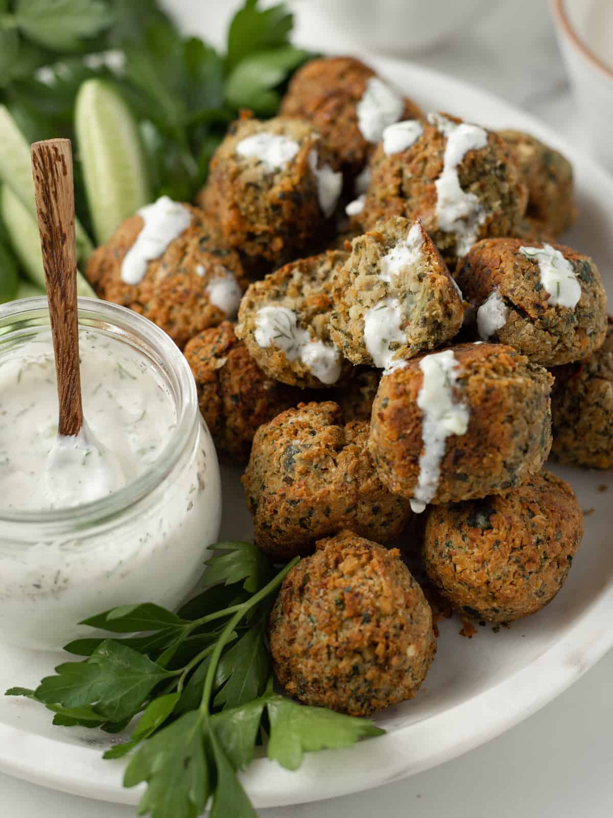 Falafel and cucumber slices on a platter with tzatziki sauce.