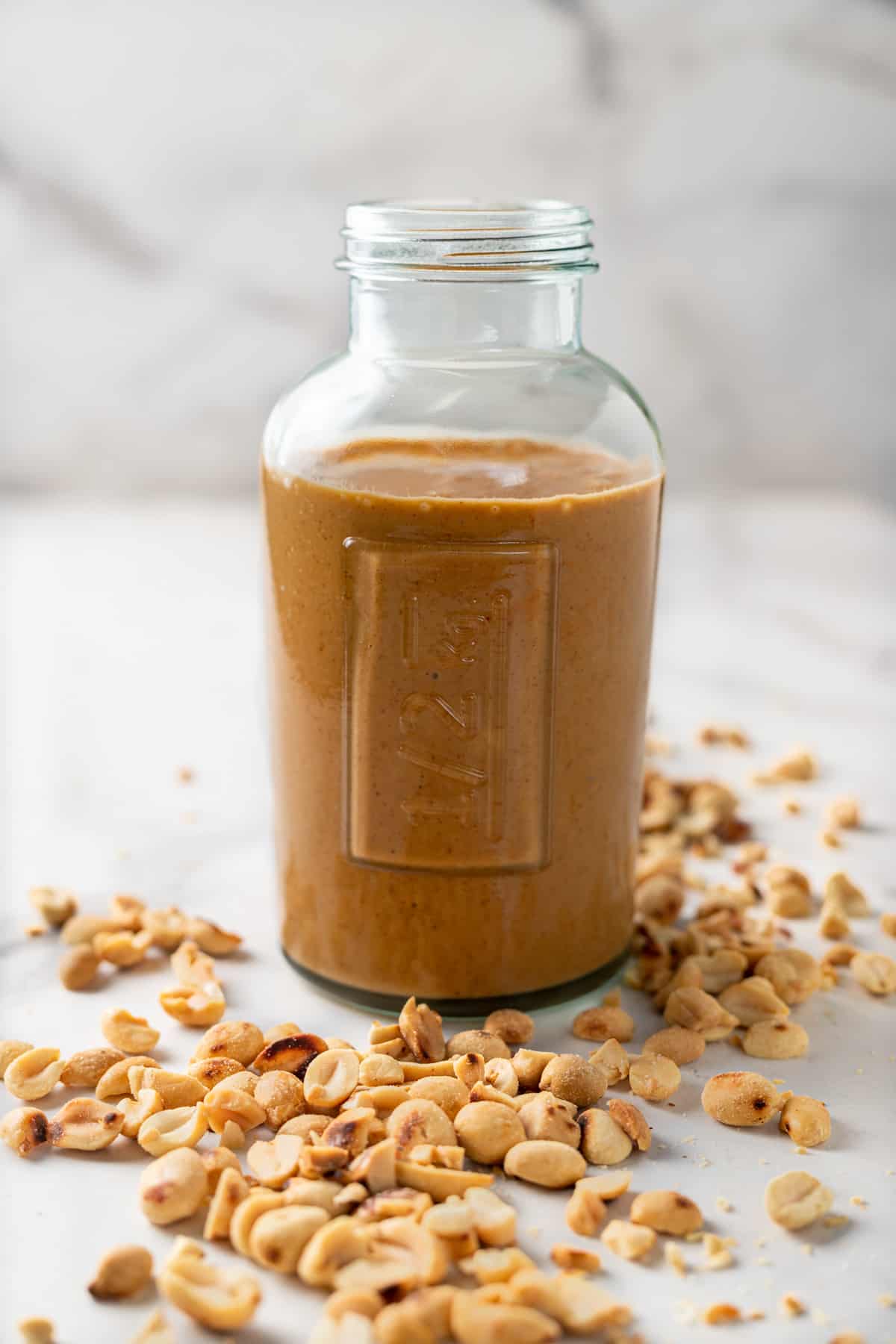 Jar of peanut sauce surrounded by a scattering of roasted peanuts.