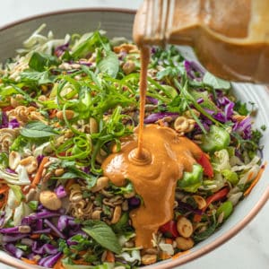 Peanut ginger sauce being pouring on a Thai crunch noodle salad.