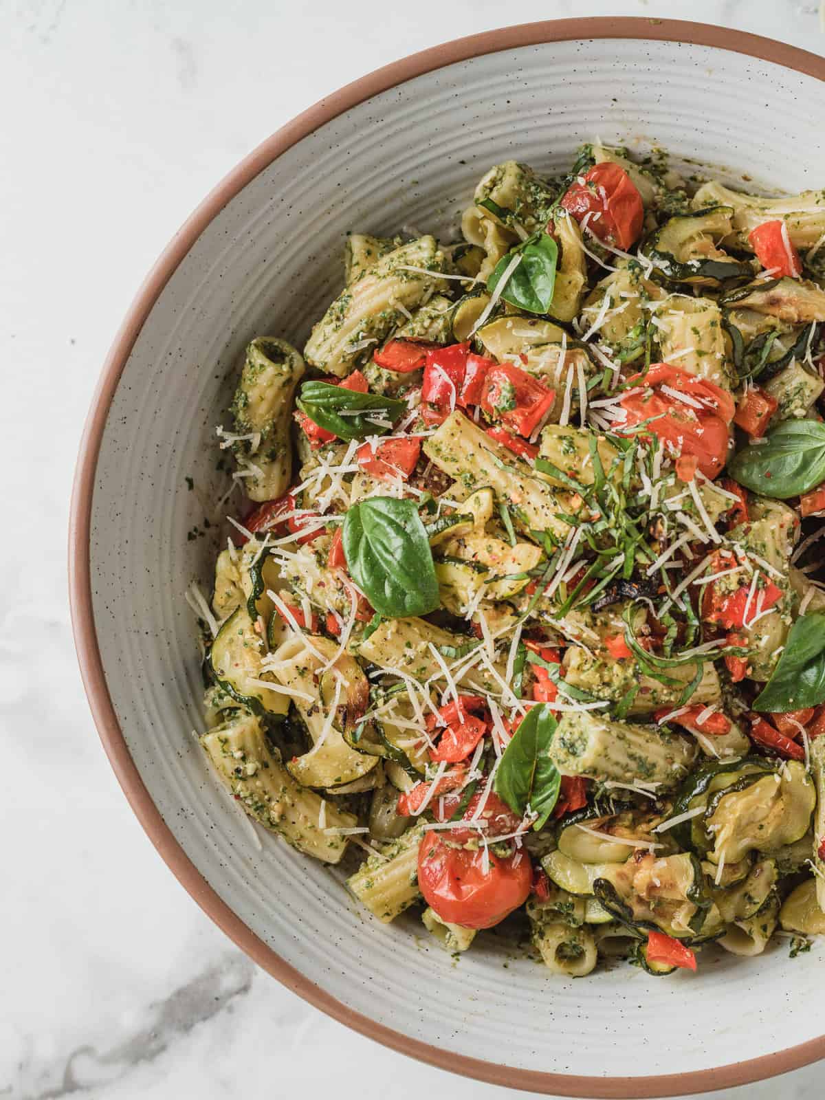 Bowlful of pesto veggie pasta with tomatoes and zucchini.