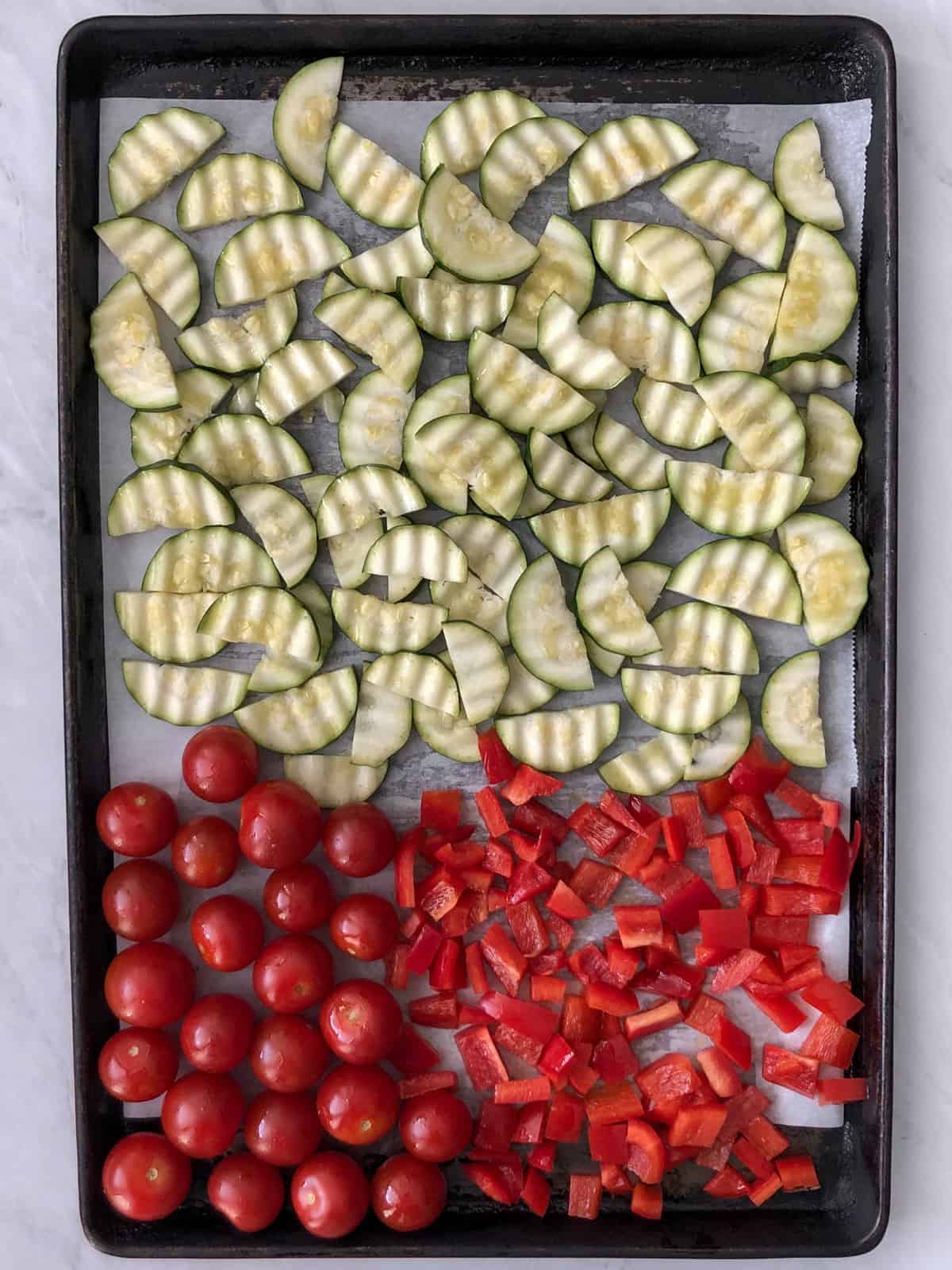 Slices of zucchini, cherry tomatoes and diced red pepper on a baking sheet.