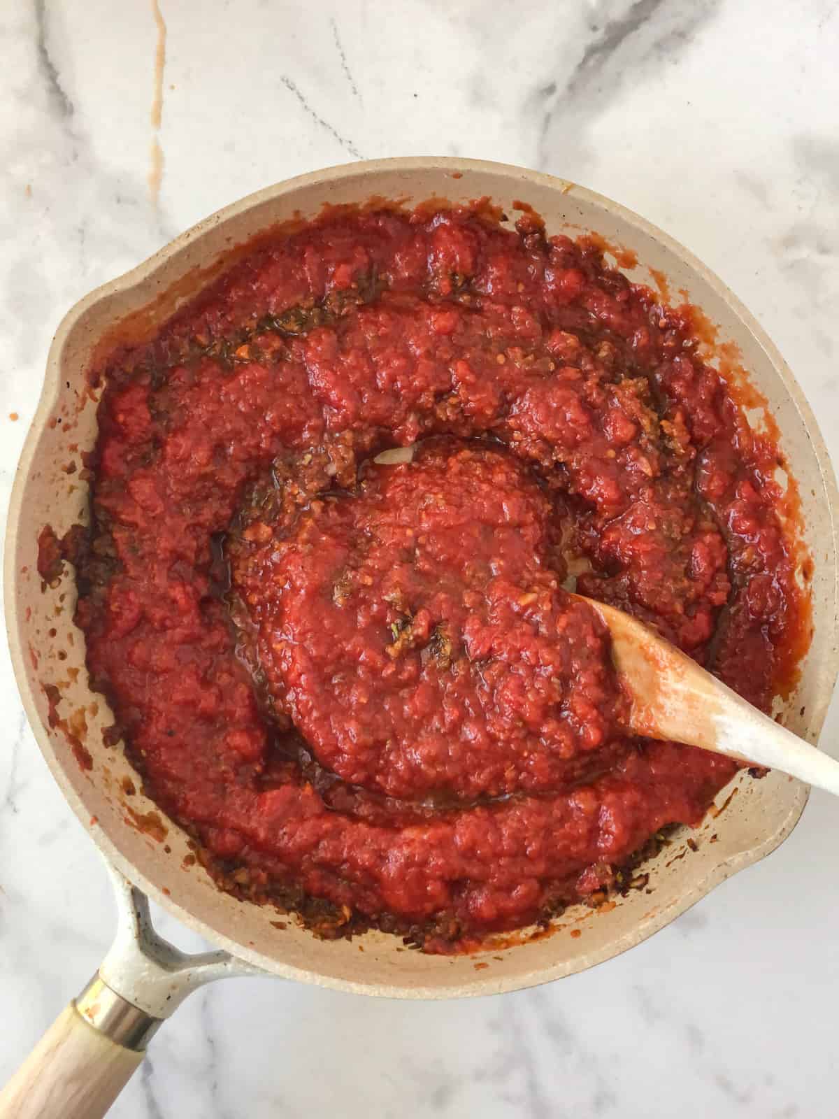 Tomato sauce being stirred in a saute pan.