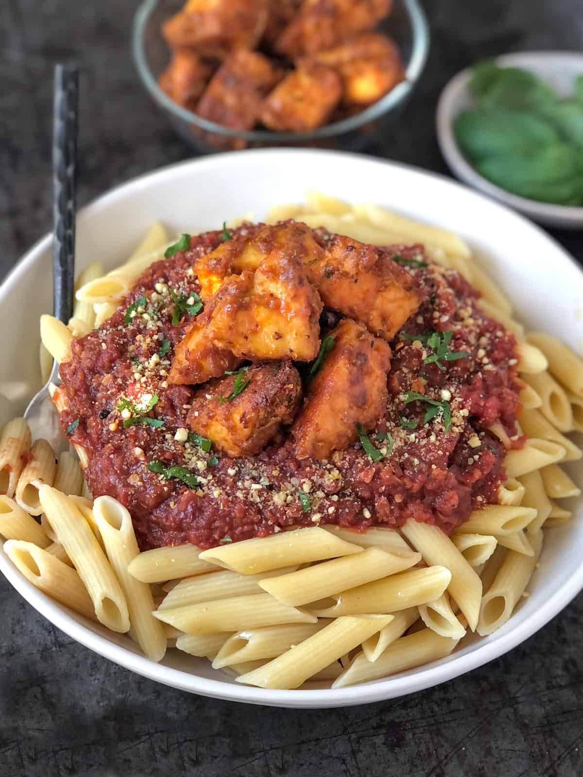 Bowlful of penne pasta topped with tomato sauce and baked tofu.