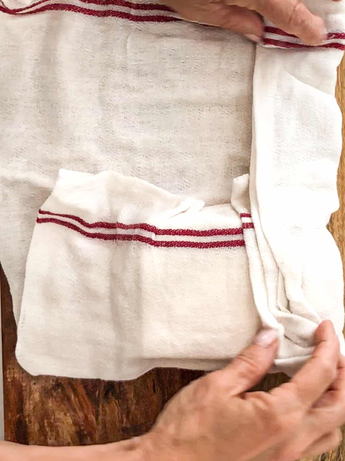 Tofu block being wrapped in a kitchen towel.