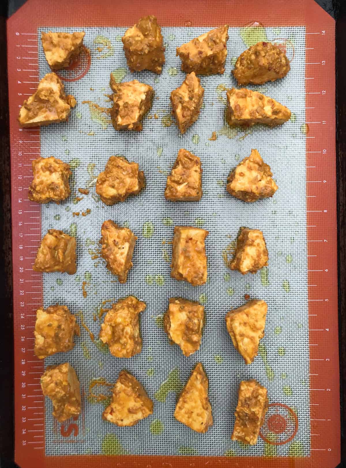 Baking sheet with spicy coated unbaked tofu chunks.