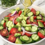 Balsamic dressing being poured on tomato cucumber avocado salad.