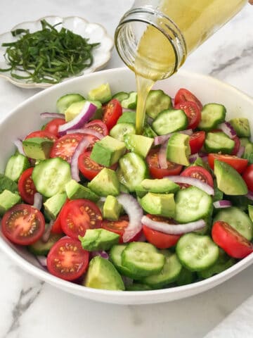 Balsamic dressing being poured on tomato cucumber avocado salad.