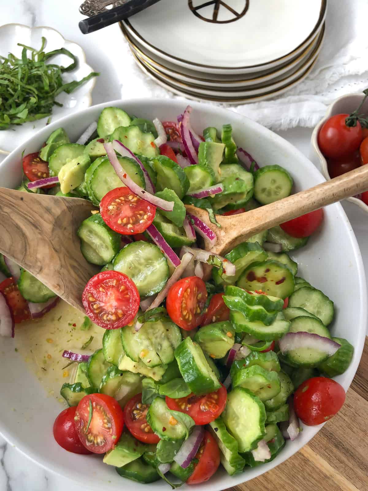 Tomato cucumber salad with avocado being tossed in a bowl. 