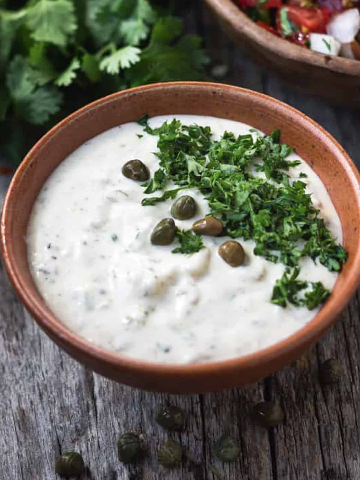 Bowl of vegan tartar sauce topped with chopped parsley and capers.