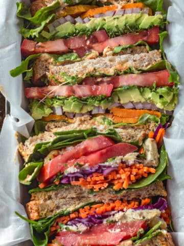 Sliced vegetable sandwiches stacked together in a tin.