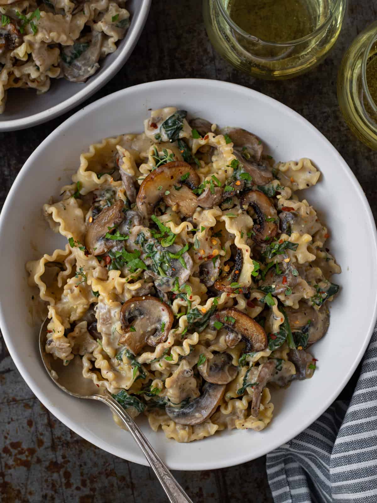 Bowl of creamy mushrooms pasta and two glasses of white wine.