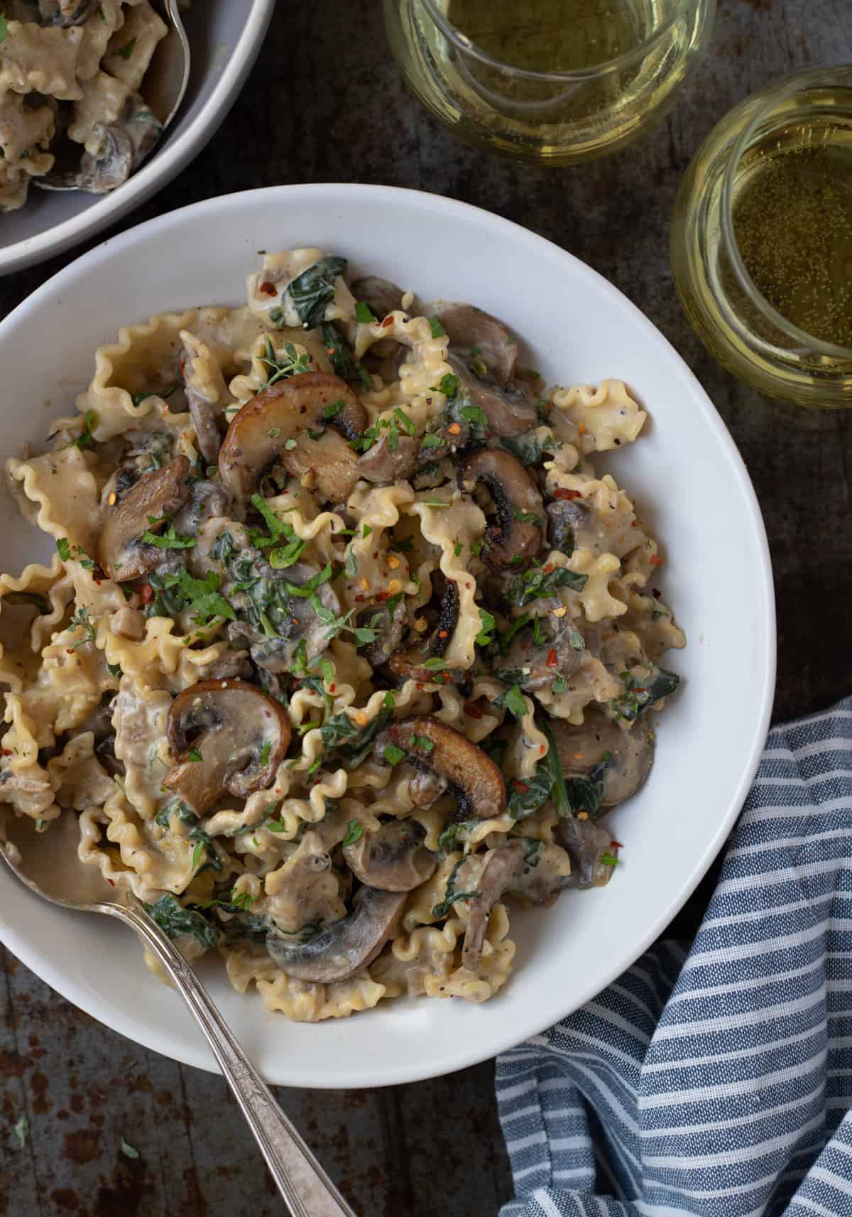 Bowlful of creamy mushroom and spinach pasta at a table setting with white wine.