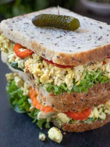 Two egg salad sandwiches with lettuce and hot peppers piled on top of each other with a pickle.