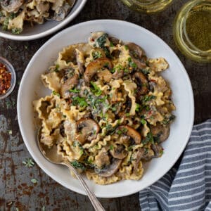 Bowlful of creamy mushroom spinach pasta with a blue and white striped napkin and a glass of wine.