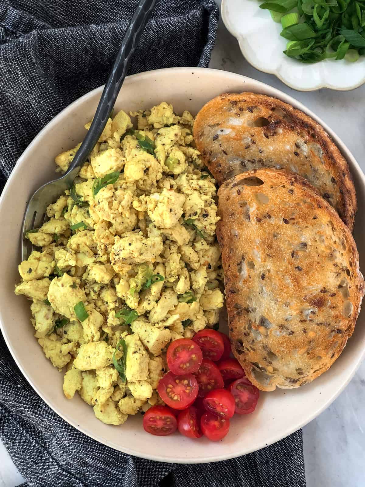 Tofu scrambled eggs and toast with tomatoes on a plate.