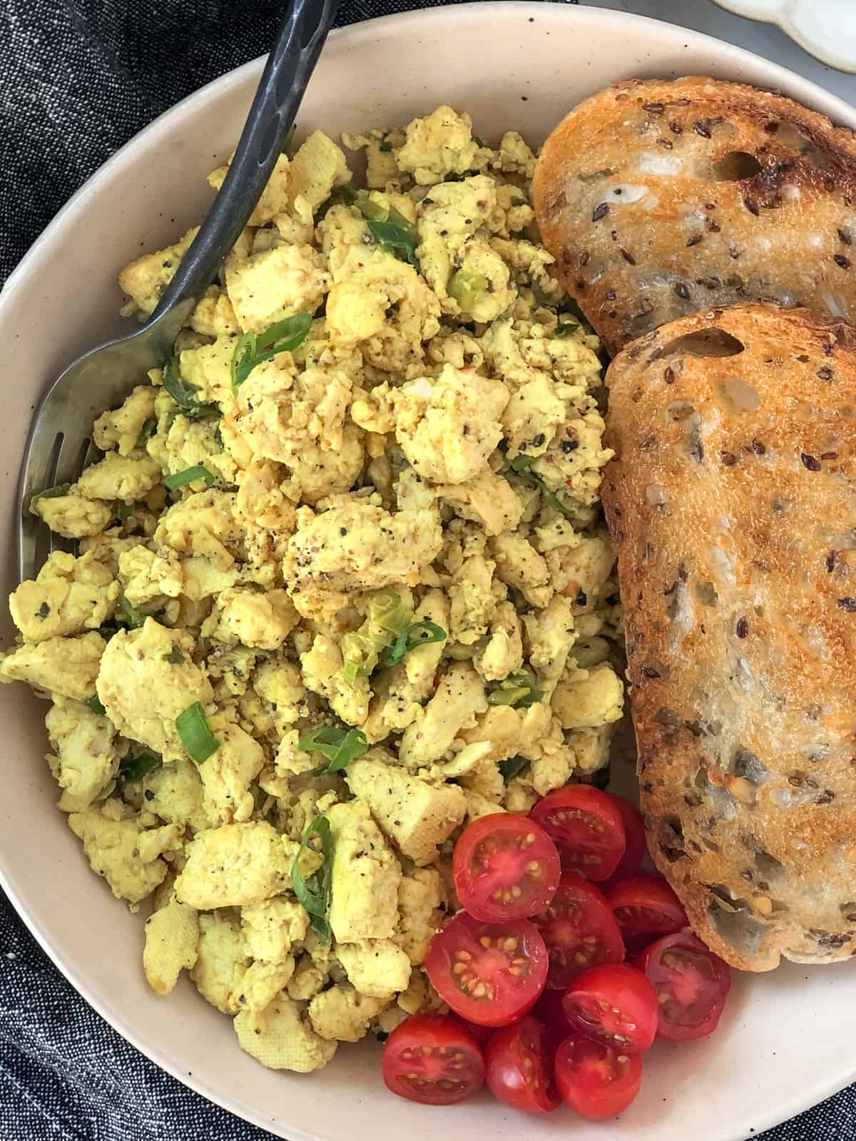 Tofu scrambled eggs and toast with tomatoes on a plate.