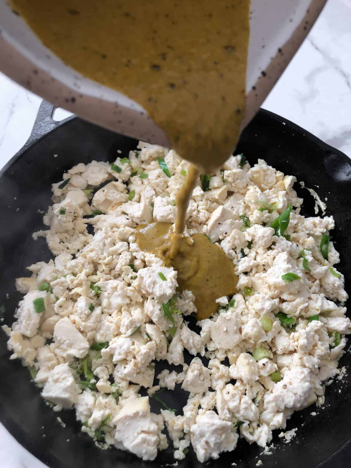 Tofu scramble seasoning being poured into scrambled eggs in a skillet.
