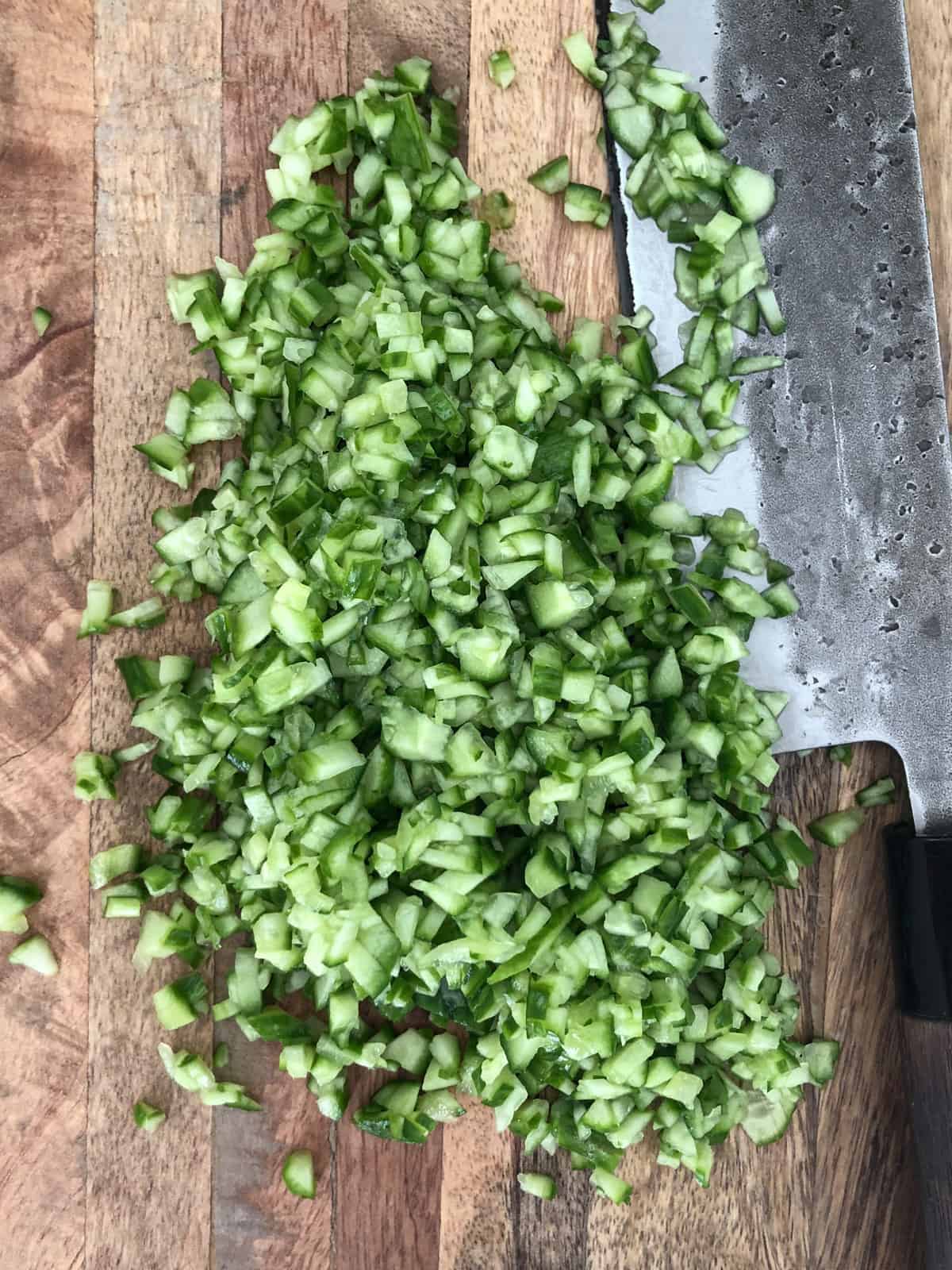 Diced cucumbers on a cutting board with a knife.