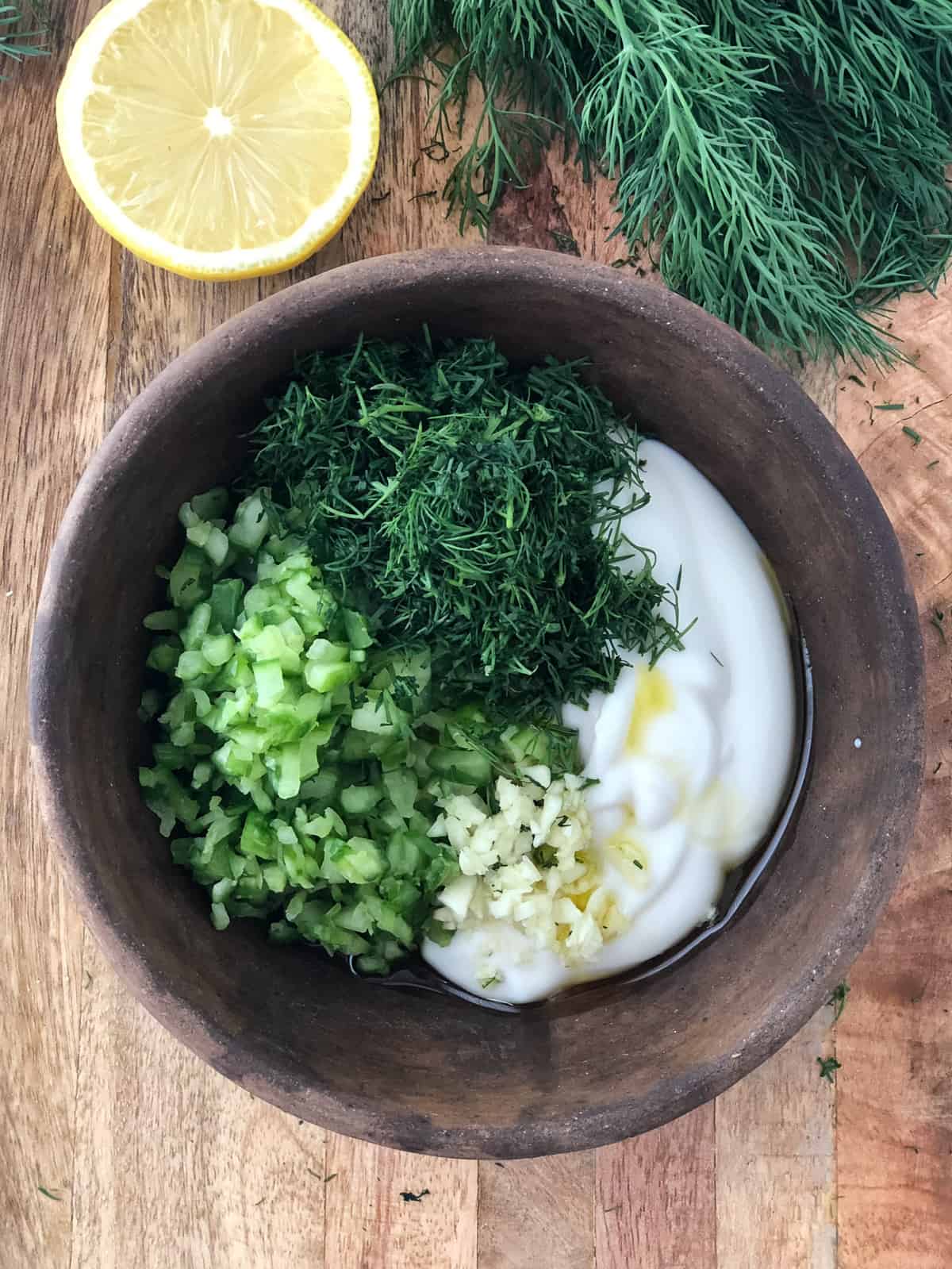 Yogurt, diced cucumbers, chopped dill and garlic in a bowl.