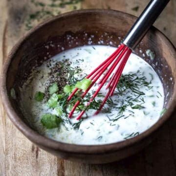 Vegan tzatziki sauce in a bowl with a red whisk.