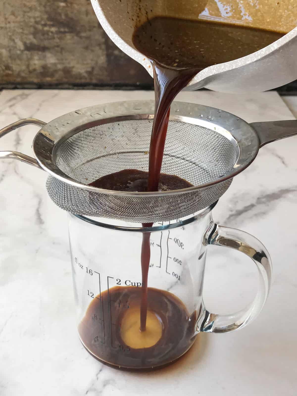 Worcestershire sauce being strained into a glass measuring cup.