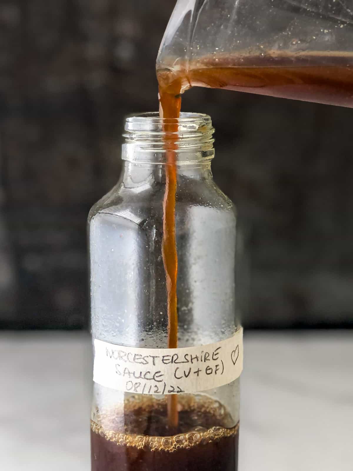 Worcestershire sauce being poured from glass measuring cup into glass bottle.