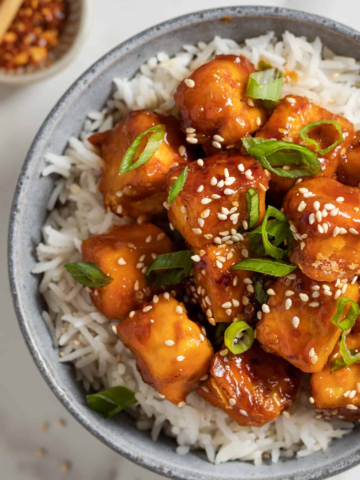 Baked tofu cubes covered in glossy teriyaki sauce in a bowl of rice.