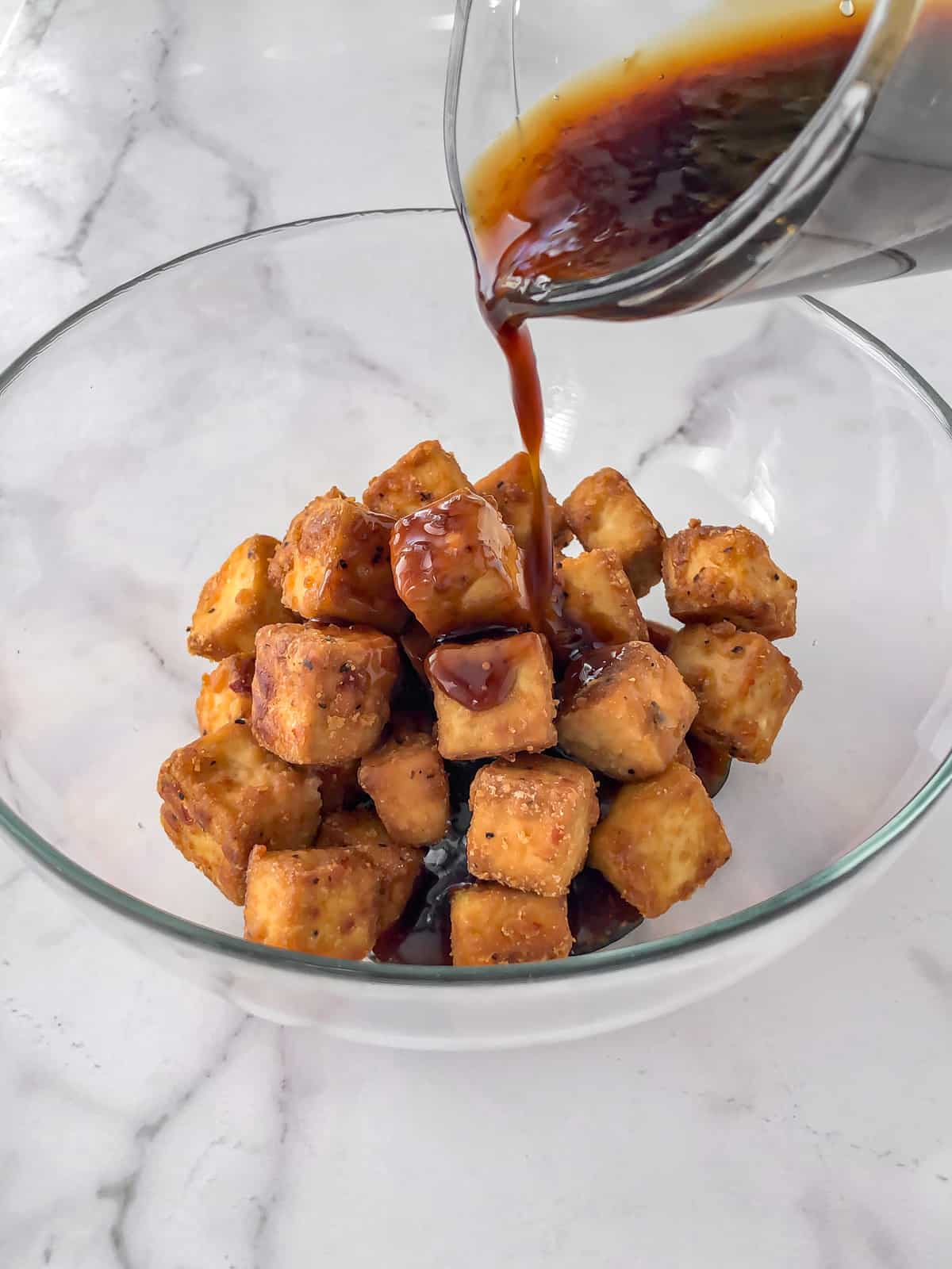 Teriyaki sauce being poured into a bowl of baked tofu.