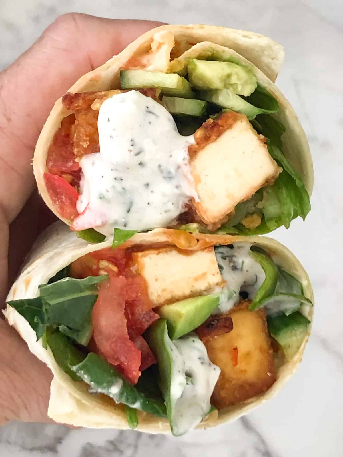 Hand holding two tofu wraps drizzled with white sauce.