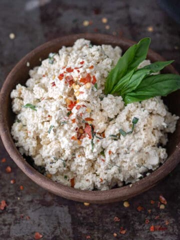 Bowl of vegan ricotta cheese topped with basil leaf.