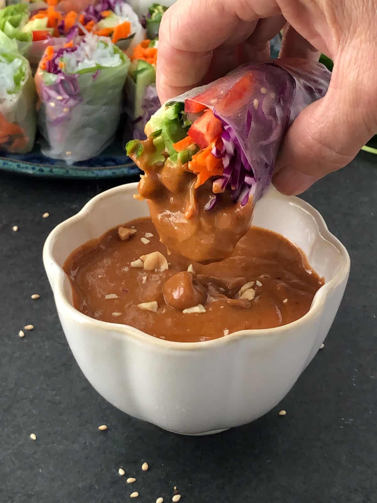 Vegetarian salad roll being dipped in peanut sauce.