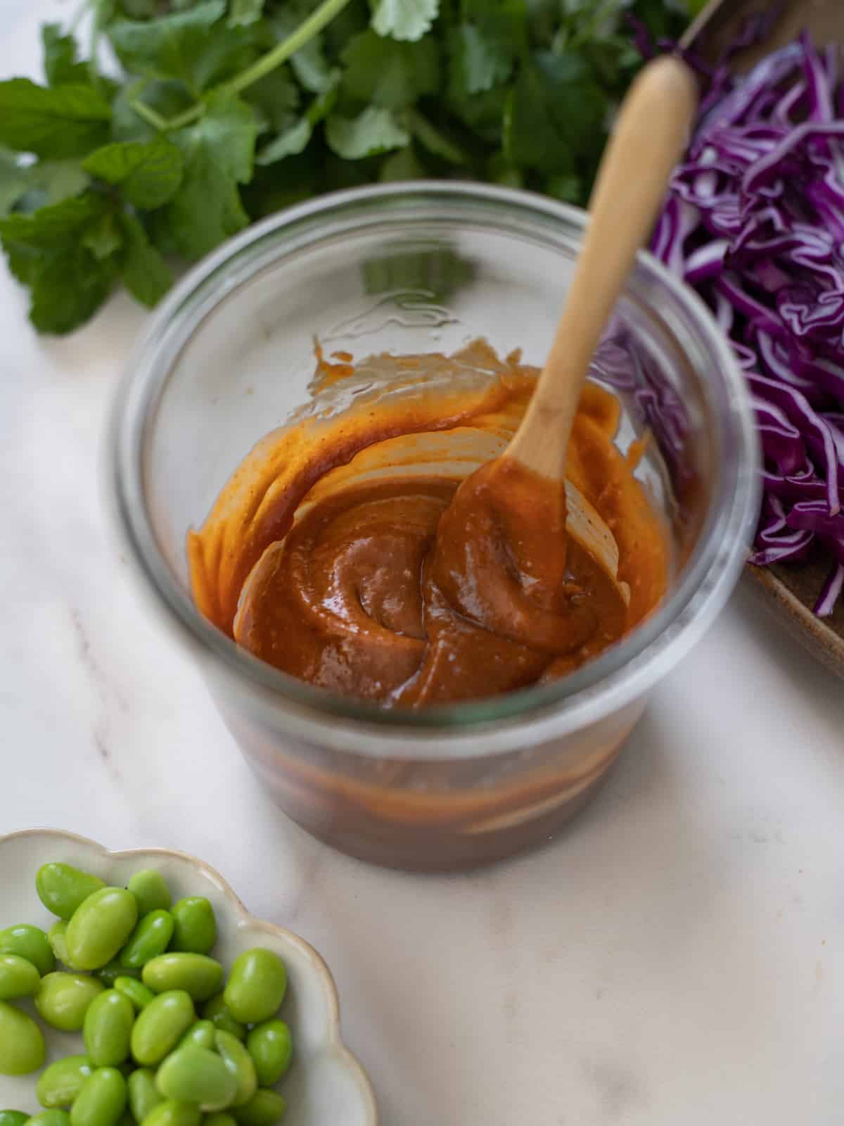 Small wooden spoon in jar of peanut hoisin sauce. 