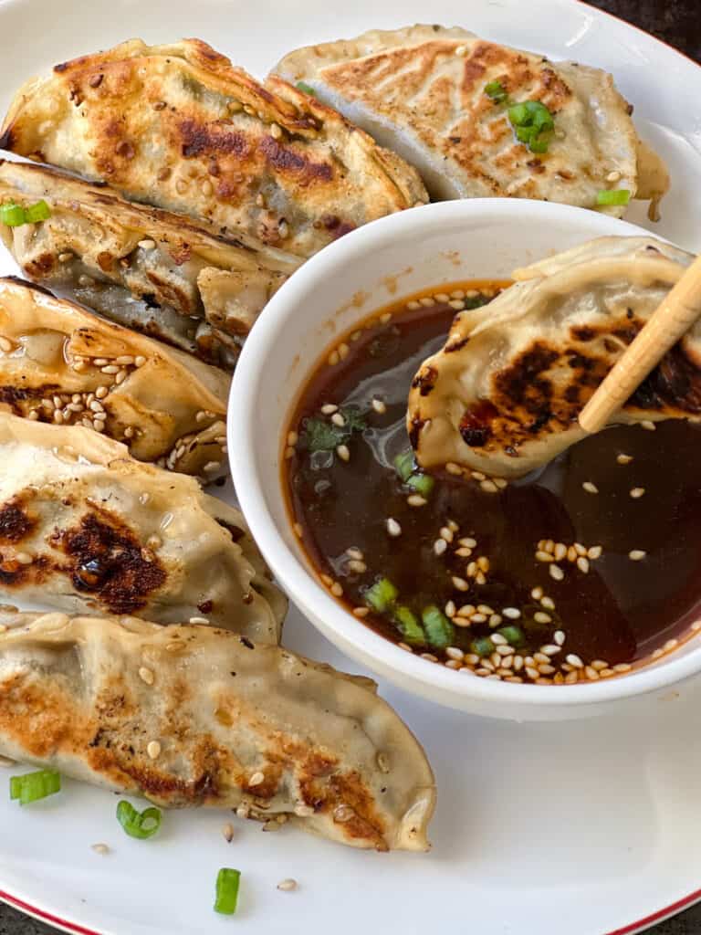 Dumpling being held by chopsticks being dunked in soy sauce.