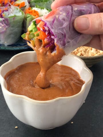 Salad roll being dipped in hoisin peanut sauce.
