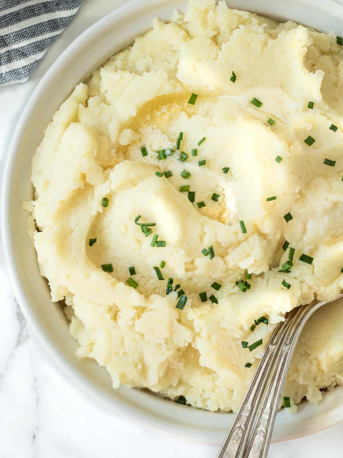 Bowl of mashed potatoes with chives sprinkled on top.