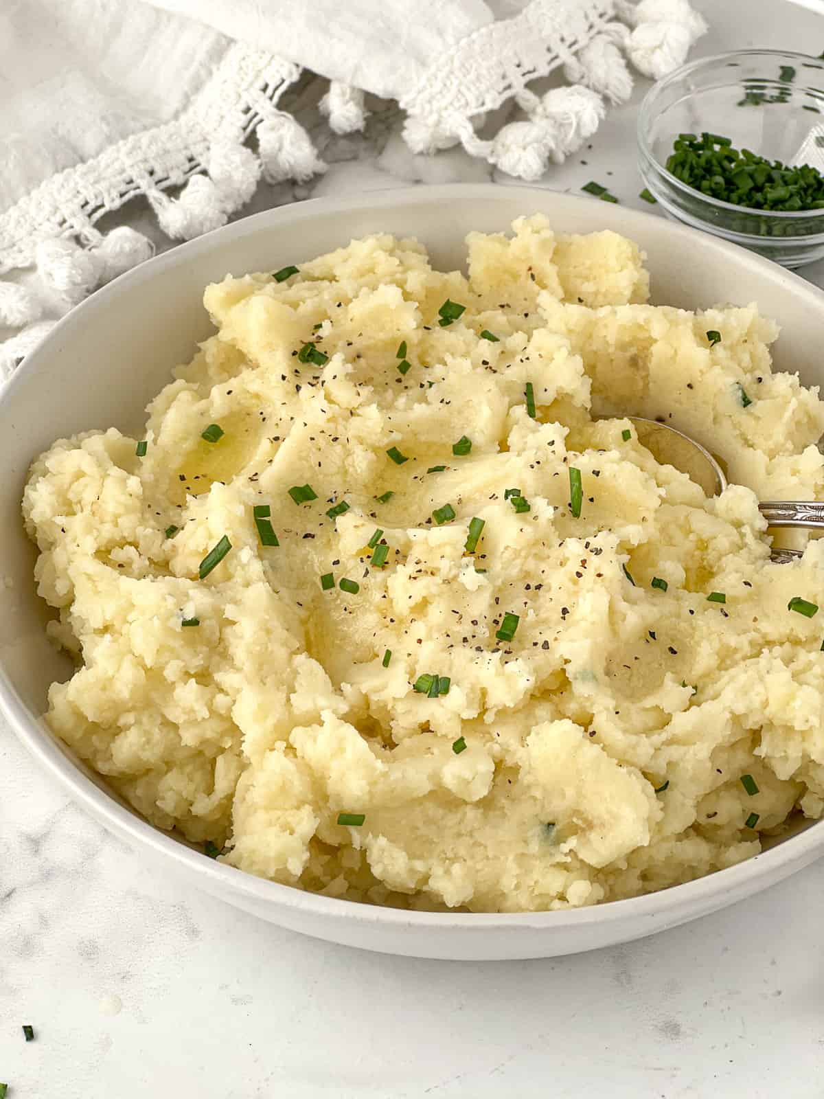 Bowlful of mashed potatoes topped with butter and chopped chives.