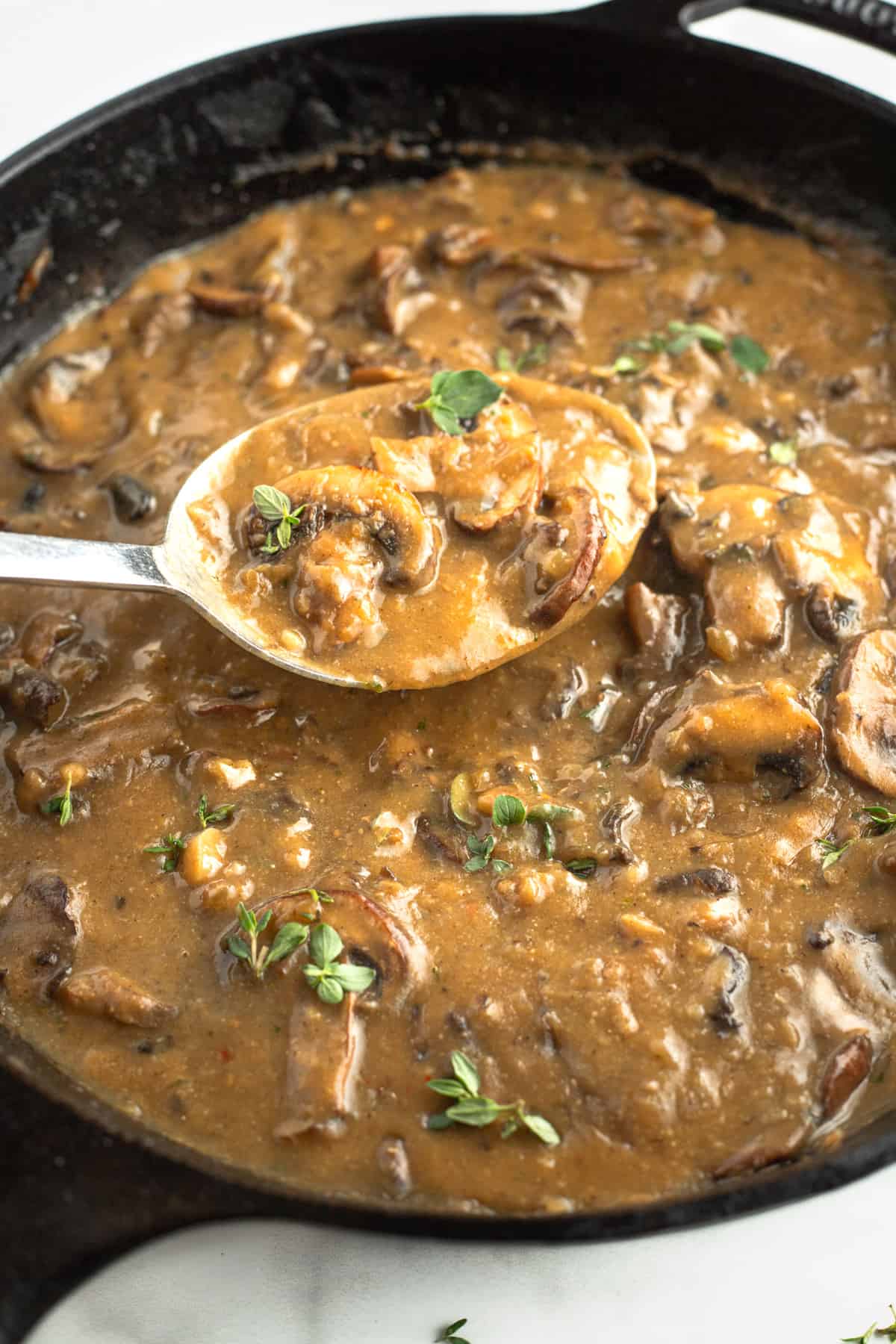 Spoonful of gravy being lifted over a skillet of mushroom gravy.