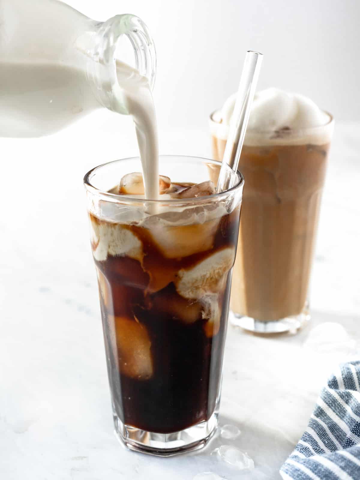 Heavy cream being poured into Vegan Iced Coffee.