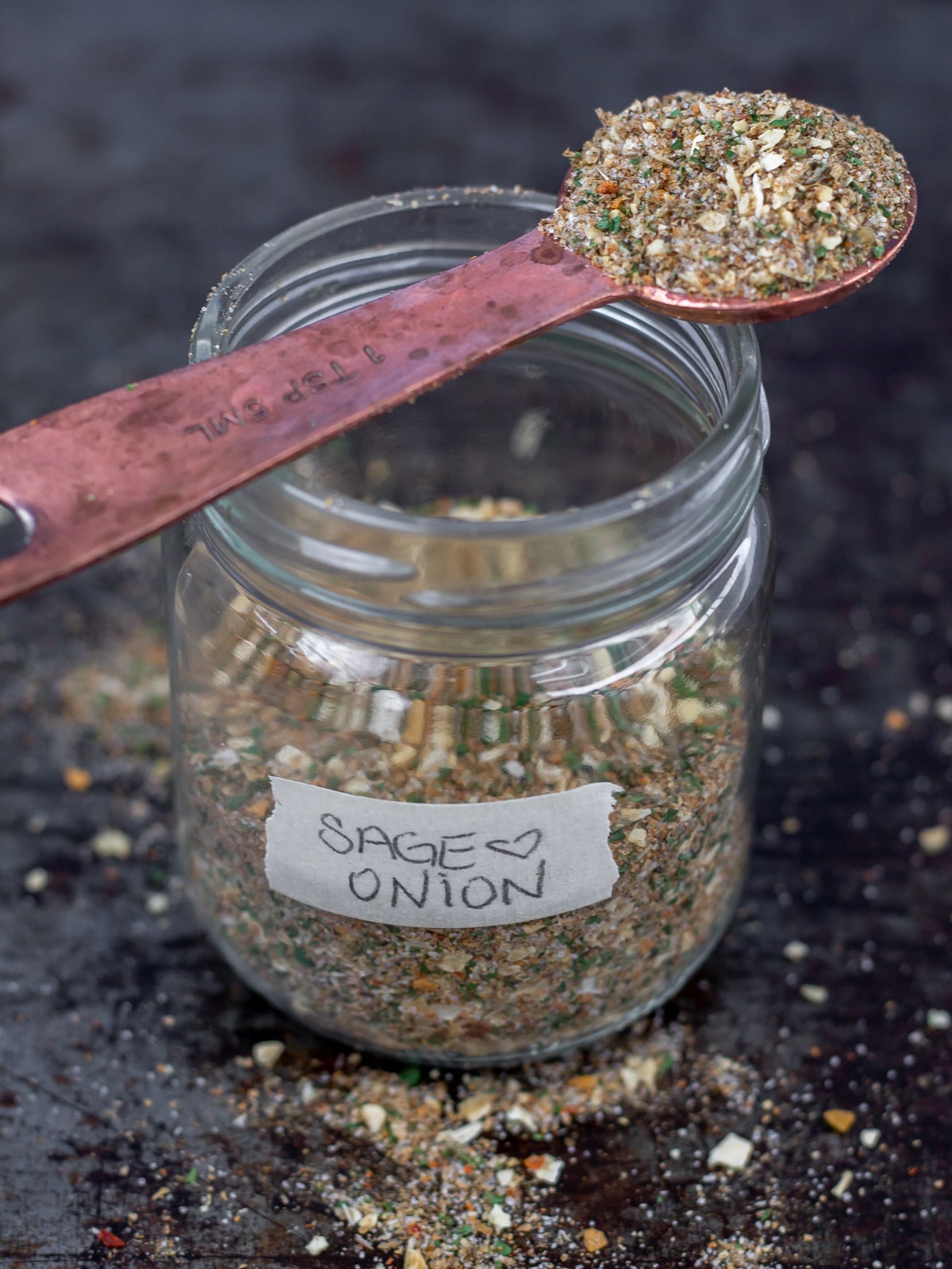 Jar of sage and onion seasoning with measuring spoon on top.