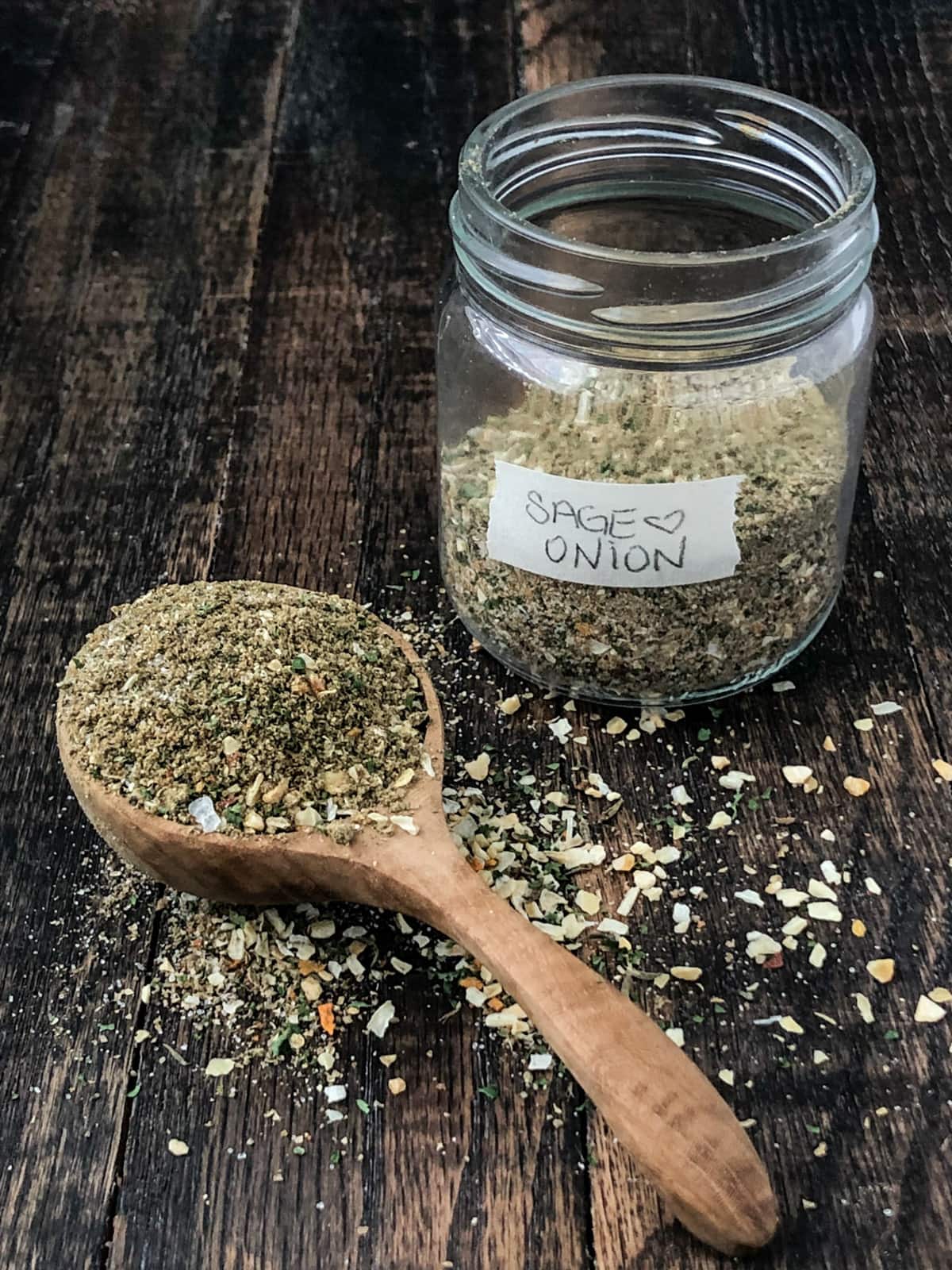 Mixture of sage and poultry seasoning spices in a jar and large wooden spoon.
