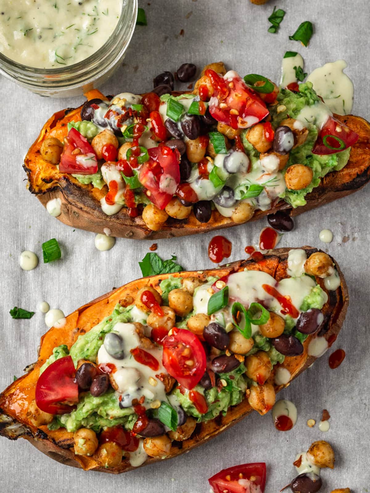 Two halves of sweet potatoes topped with chickpeas, black beans, avocado and sauce.