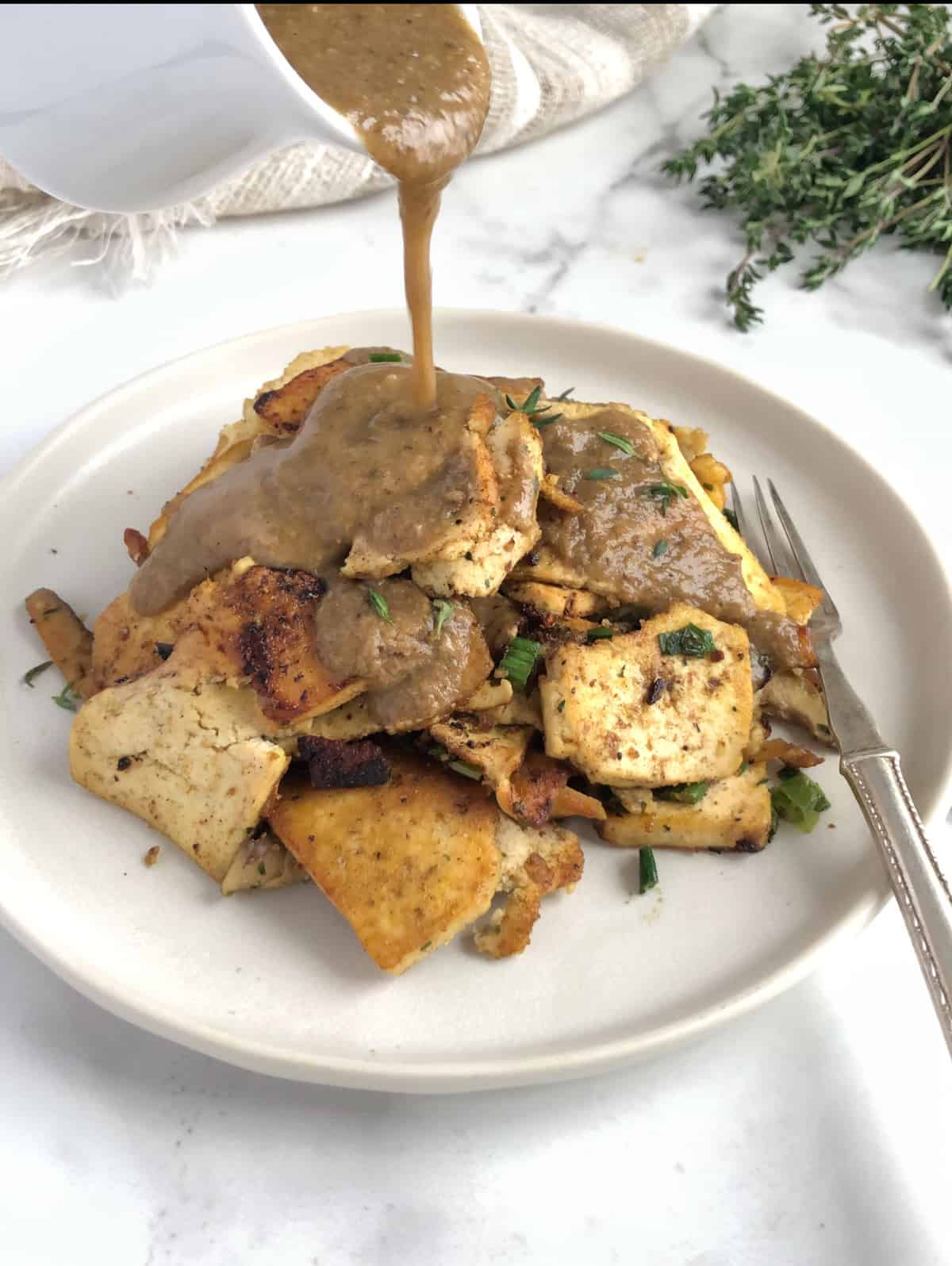 Gravy being poured onto a pile of turkey slices on a white plate with a silver fork.