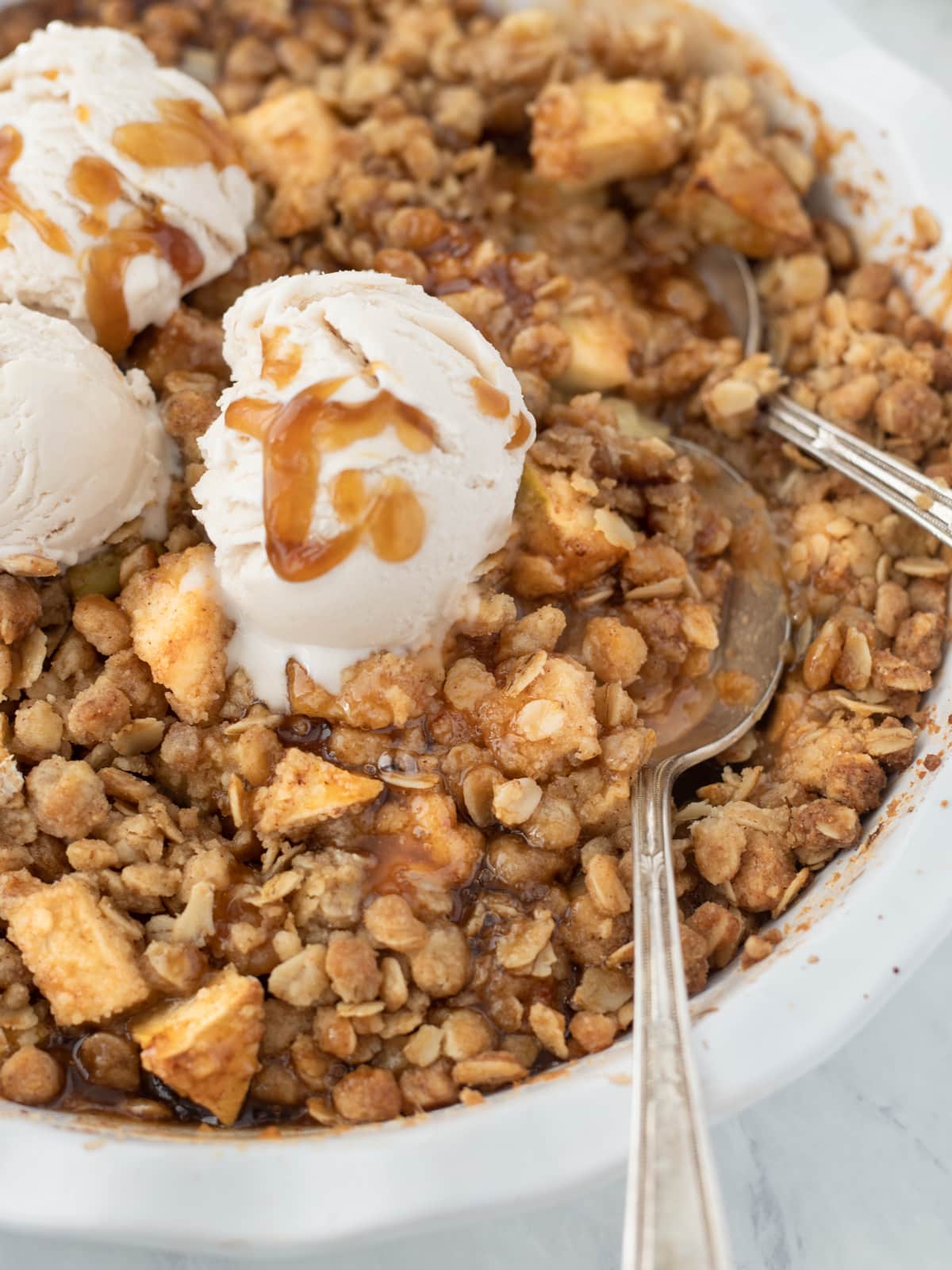 Close up shot of pan of apple crisp topped with scoops of ice cream.
