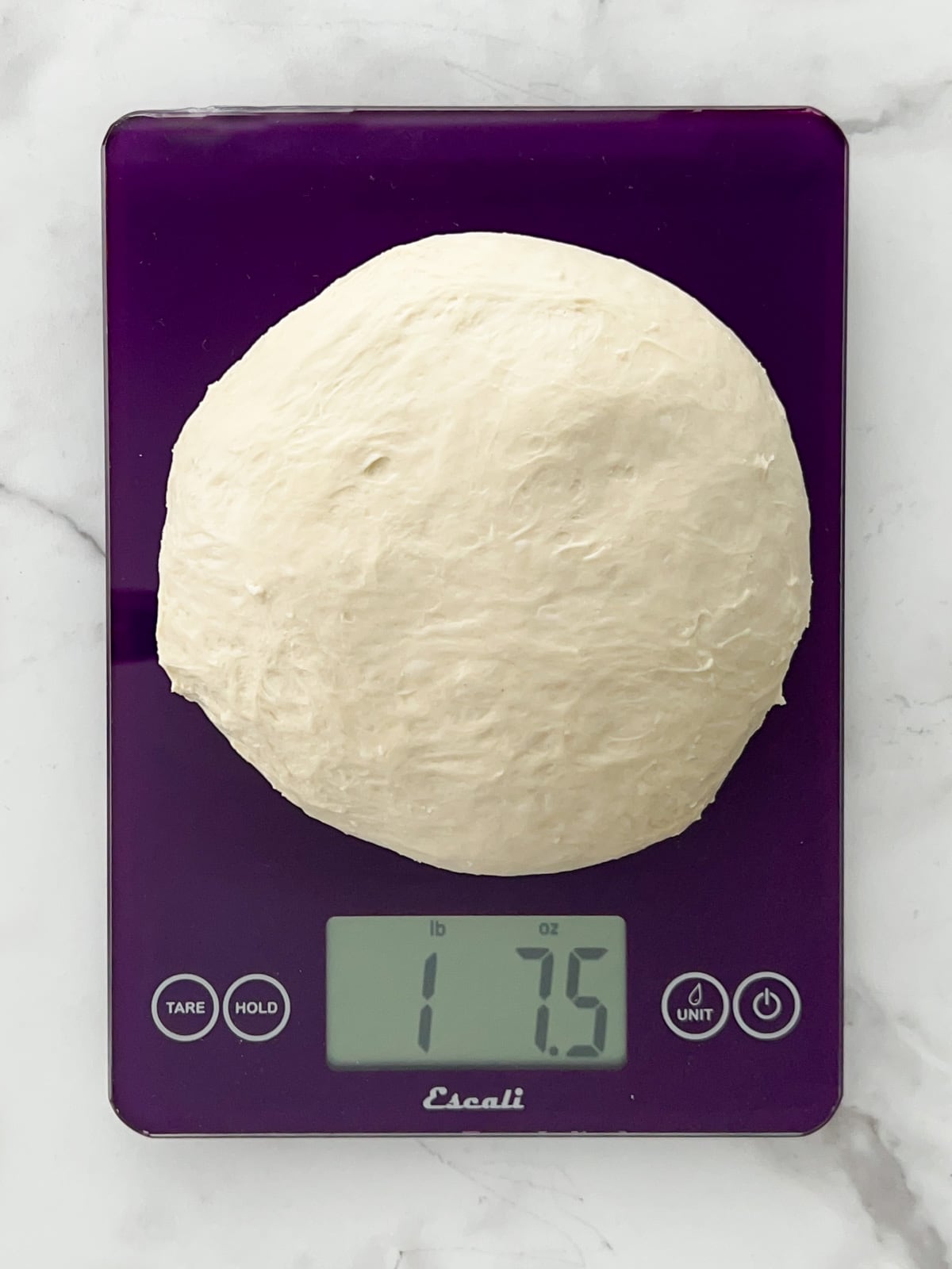 Bread dough being weighed on a purple kitchen scale.