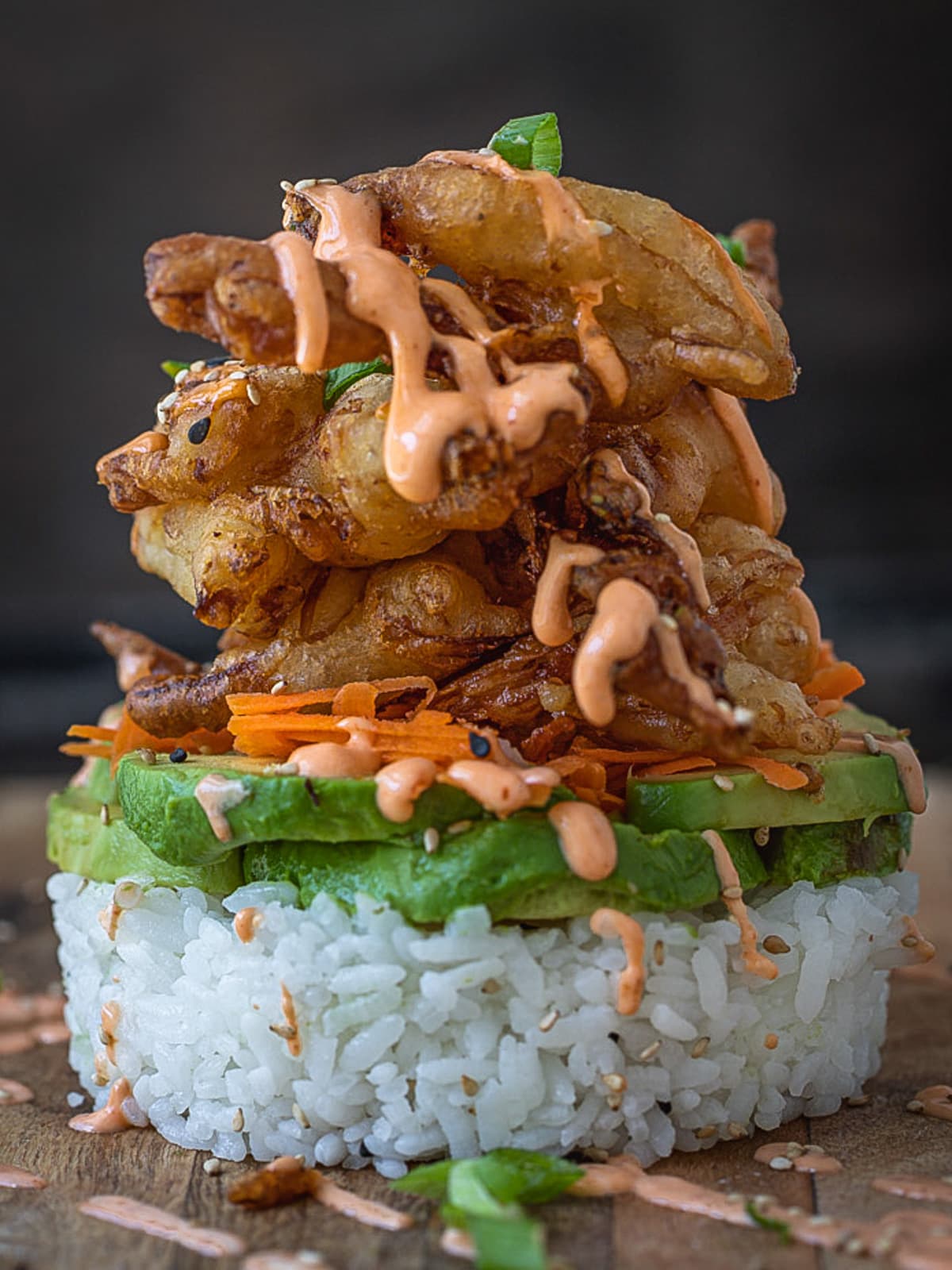 Spicy dynamite roll and avocado stacked on rice with spicy sushi sauce drizzle.